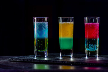 Cocktails Party Shots and Shooters on bar counter in a restaurant, pub. Miniature mixed drinks. Alcoholic cooler beverage at nightclub on dark background