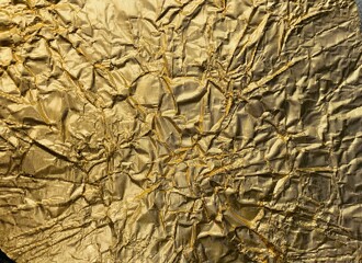 The golden shimmering surface of a metal foil with folds
