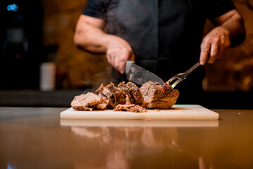 Selective focus on delicious fried meat which man cuts to slices on cutting board.
