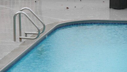 Rain drops falling on water surface of blue swimming pool, rainy day in motel or hotel, California...