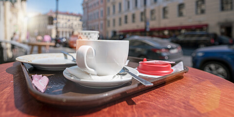 Empty white cup and plate with tea spoon on table of street cafe. Breakfast and fastfood concept.
