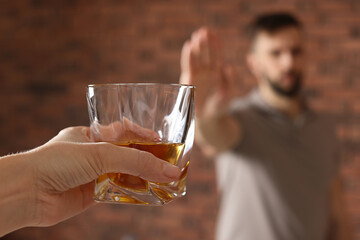 Man refusing to drink whiskey near red brick wall, closeup. Alcohol addiction treatment