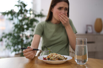 Young woman feeling nausea while eating at wooden table indoors. Toxicosis during pregnancy