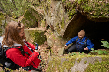 Woman hiker watching man leaving cave in rock