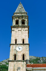 Perast town, Montenegro - 16 october 2021 : Clock tower in Perast sailor and fisherman village or town on Adriatic coast, blue sky, stone ancient architecture, middleage cultural heritage