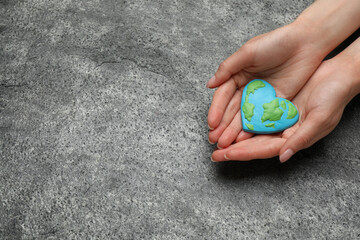 Happy Earth Day. Woman with heart shaped plasticine planet at grey table, top view and space for text
