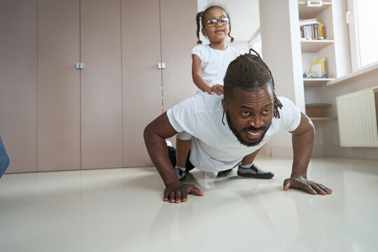 Adult African American father doing push-ups with his daughter on his back