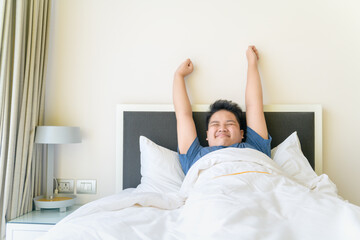 Obese boy wake up and stretch arm on bed in morning. lazy concept