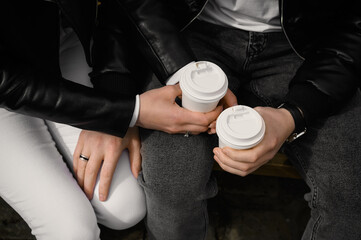 Lovely couple with coffee holding hands together while sitting on bench outdoors, closeup. Romantic date