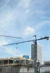 Tower crane near unfinished building against cloudy sky