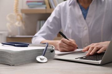 Doctor making notes from laptop at table indoors, closeup. Medical education