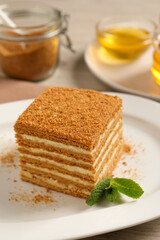 Fototapeta na wymiar Slice of delicious layered honey cake with mint on plate, closeup
