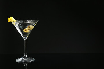 Martini cocktail with olives and lemon twist on dark background, space for text