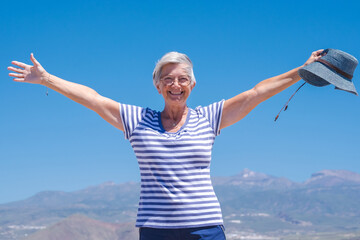 Happiness and good mood in senior smiling woman with outstretched arms in outdoors excursion. Attractive white haired lady dressed in blue expressing freedom and joy