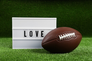 American football ball and lightbox with word Love on green grass