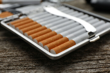 Silver case with tobacco filter cigarettes on wooden table, closeup
