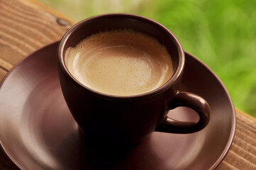 A cup of aromatic coffee with foam on a background of green grass. Close-up.