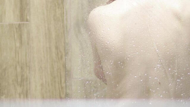 naked woman turned with the back is taking shower after a glass wall. young woman, girl, morning routine. cleaning body, refreshing, body and skin care.
beauty concept.
unrecognizable face. water pour