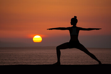 Woman silhouette in Yoga Warrior pose at sunset with quiet ocean