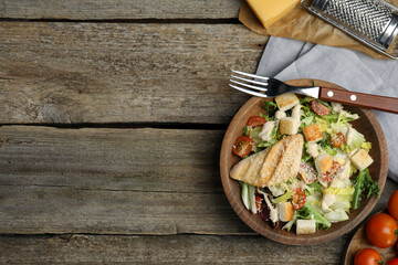 Delicious Caesar salad in bowl on wooden table, flat lay. Space for text