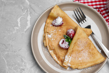 Delicious crepes served with mint, raspberries and powdered sugar on grey table, top view