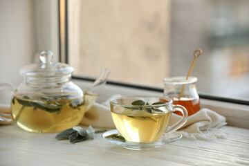 Sage tea and green leaves on white wooden windowsill