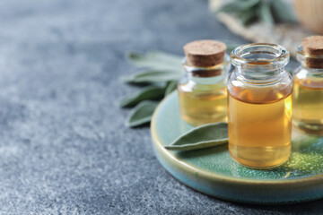 Bottles of essential sage oil and leaves on table, closeup. Space for text