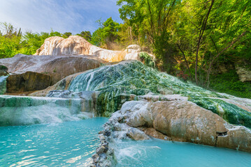 Naklejka premium Geothermal pool and hot spring in Tuscany, Italy. Bagni San Filippo natural thermal waterfall in the morning with no people. The White Whale amidst forest.