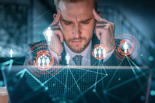 Handsome businessman in suit at workplace working with laptop to hire new employees for international business consulting. HR, social media hologram icons over office background