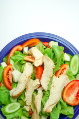 Salad with difference lettuce tomato and baked chicken breast on blue dish