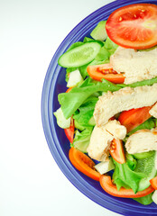Salad with difference lettuce tomato and baked chicken breast on blue dish