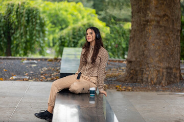 Attractive teen girl sitting in a park with headphones and having coffee.Copy space