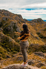 Naklejka premium Portrait of latin woman having fun during trekking day in mountain forest posing on a rock- Back focus