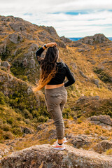 Naklejka premium Portrait of latin woman having fun during trekking day in mountain forest posing on a rock- Back focus