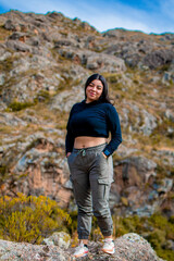 Naklejka na ściany i meble Portrait of latin woman having fun during trekking day in mountain forest posing on a rock- Front focus
