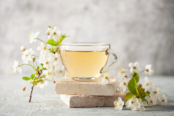Hot tea in glass cup and blossom cherry flowers on stone podium. International tea day