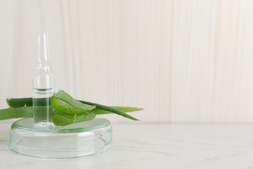 Pharmaceutical ampoule with medication and aloe leaves on white table, space for text
