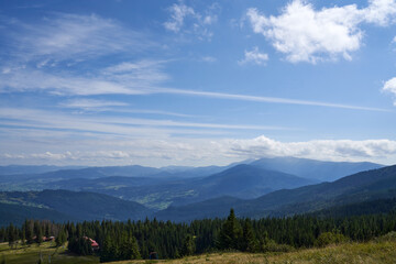 Breathtaking landscape of mountains and hills in Carpathians, Ukraine. Above view of grassy mountain slope with single houses in dense coniferous forest in summer, copy space. Concept of travelling.