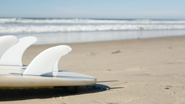 Surfboard for surfing lying on beach sand, California coast, USA. Ocean waves and white surf board or paddleboard. Longboard or sup for watersport recreation by sea water. Seamless looped cinemagraph.