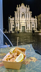 Eating fried calamaris with lemons at night on the main square of Catania in Sicily, Italy, Europe....