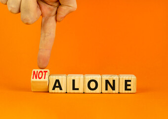 You are not alone symbol. Businessman turns wooden cubes and changes concept words alone to not...