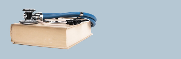Banner with medical education concept. Book with stethoscope on blue background. Learning information about medicine, health care, treatment. Copy space. High quality photo