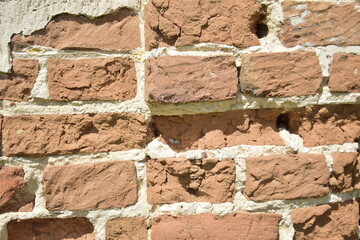 A wall of old, cracked bricks, with a weathered and faded surface. Restored brickwork of an old house.