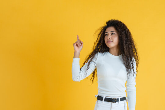 Young woman in white pointing upwards on yellow background