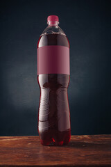 Red soda pop bottle with blank label on dark wooden background, template mockup no brand advertising, fresh berry drink