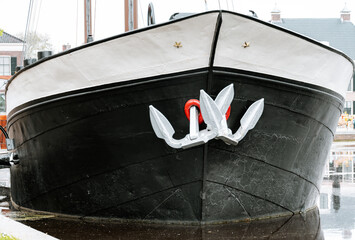 A silver anchor on the black bow of an old barge © Joanna