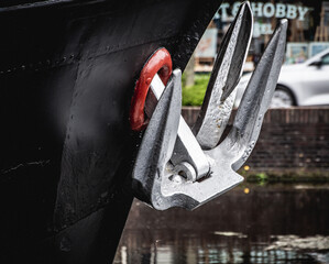 A silver anchor on the black bow of an old barge © Joanna
