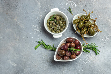 Caper berries and olives on white plate with fresh basil leaves on a gray background. Mediterranean snack assortment. banner, menu, recipe place for text, top view