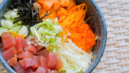 Close up of Hawaiian dish poke bowl with diced raw salmon and tuna served with fresh vegetables, seaweed. Cubed raw fish, green onions and caviar in grey bowl. Healthy organic food. Low carb diet