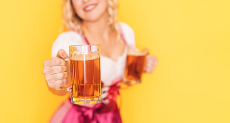 Woman in festive German dress holds out mug of beer forward.